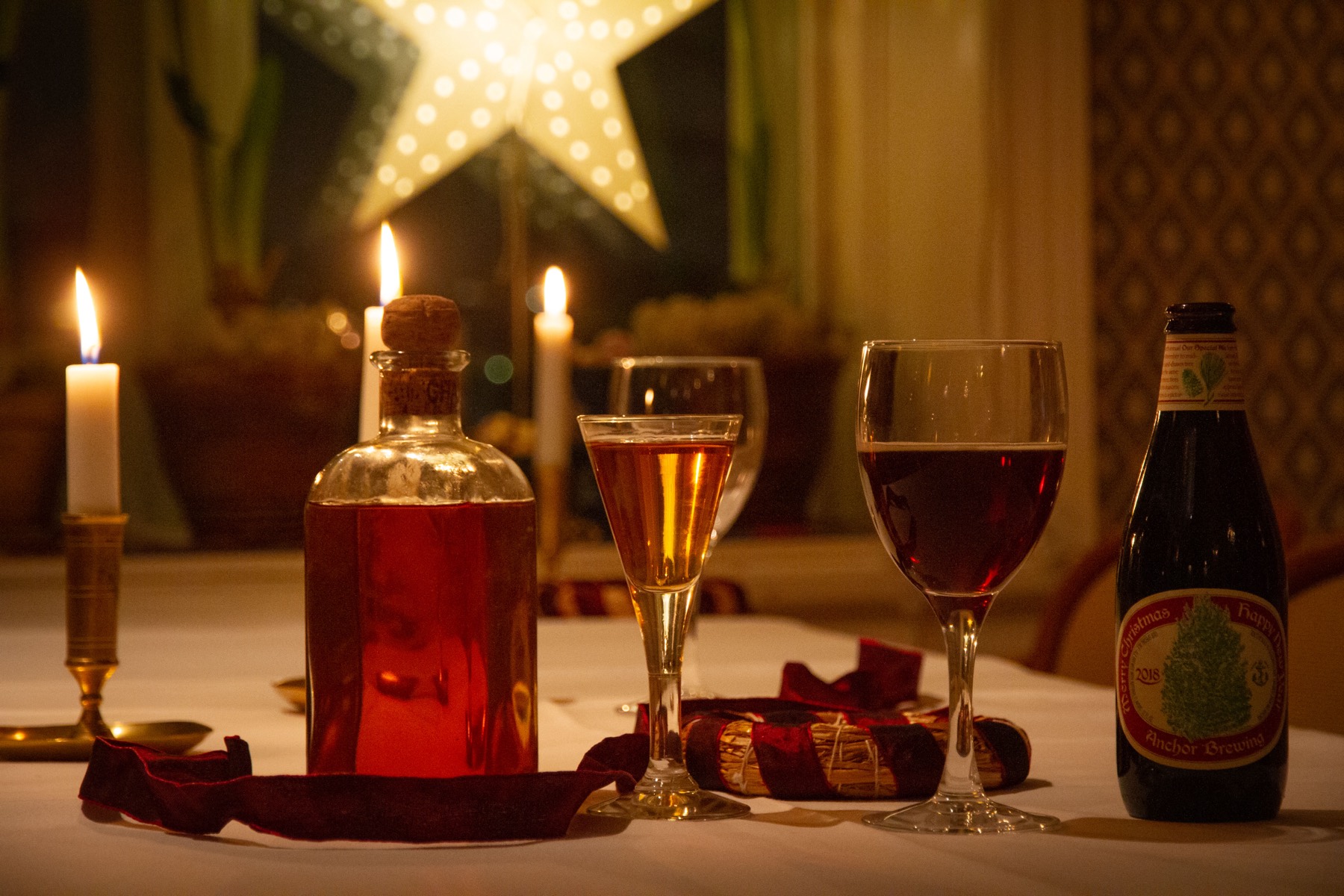 Tända ljus, en karaff, ett glas vin och en ölflaska på vit duk framför en lysande stjärna